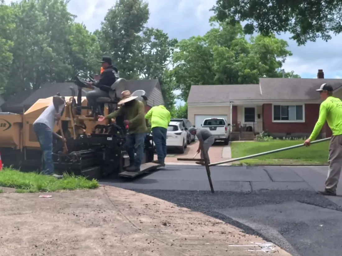 Paving crew working fresh asphalt behind the paver on a residential street