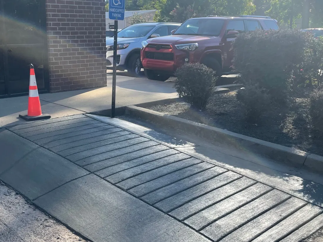 Grooved accessible ramp at a building entrance with a safety cone